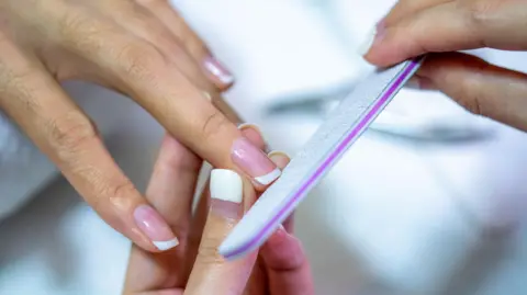 Getty Images Closeup shot of a woman in a nail salon receiving a manicure by a beautician with nail file.