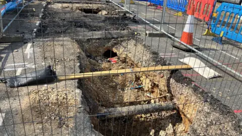 Hsin-Yi Lo/BBC Two sinkholes on a residential road. There are metal fencing and barricades around them.