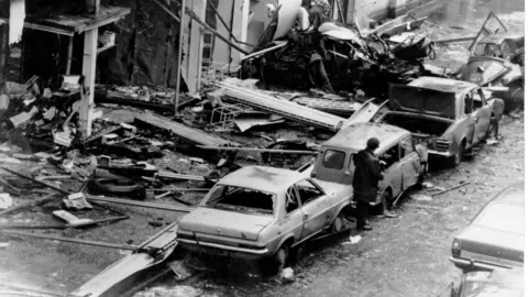 PA Media A black and white image of the aftermath of the bomb in 1974. A storefront has been completely destroyed while cars have been destroyed.