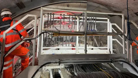 Steps inside a massive tunnel boring machine. There are two workers in hi-viz clothing on either side of the steps, which are like a bridge