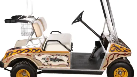 A golf buggy with a yellow, red and navy psychedelic patterned swirls painted on to it, as well as an image of wild flowers