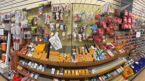 Image of the inside of a hardware shop with shelves and display racking of light bulbs and other electrical merchandise