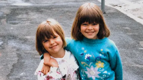 Family photo A picture takes in 1996 shows Nikita Dallison and Mellissa Arkwright standing on a pavement next to a road. A number of parked cars can be seen in the background. 