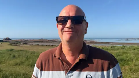 Christian Hill is pictured in Le Hocq, he is wearing sunglasses and a white and brown hooped top