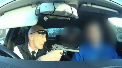 A screengrab of the video showing the driver pointing what appears to be a gun at a man in the passenger seat