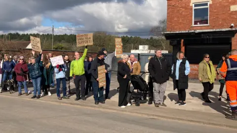 Protesters stand on a pavement, with many holding up signs such as 'No excuse for animal abuse' and 'honk to show your support'.