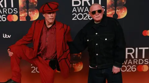 Reuters Mark "Bez" Berry (left) and Shaun Ryder of The Happy Mondays posing on the red carpet during for the 2026 Brits