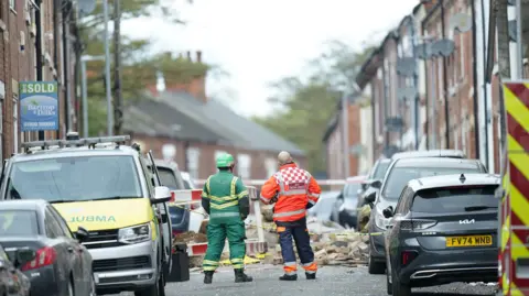 PA Media Two members of the emergency services stood in John Street following the blast