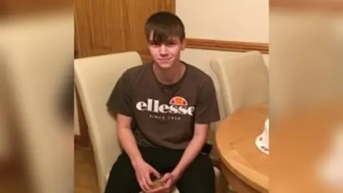 Dyfed Powys Police George Joseph Powell sitting on a cream chair, wearing a brown T-shirt and smiling into the camera 