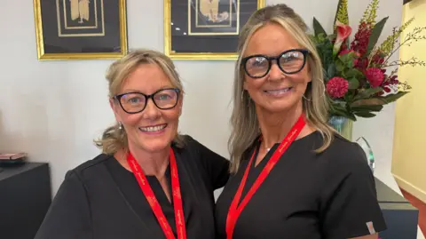 Two women wearing glasses and smiling with red landyards around their necks.