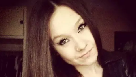 Family picture Young woman with long dark hair with striking eye makeup and a nose piercing looking straight at the camera