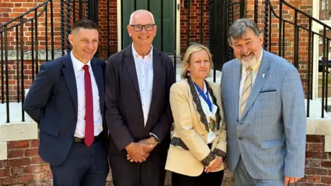 Martin McCabe, Ian Davey, Donna Johnson and Jay Mercer in formal clothing, smiling for the camera. Johnson is wearing a mayoral medallion.