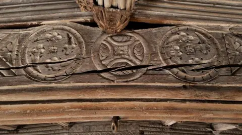 Historic England Cut marks through wooden section of ceiling showing where beetles have chomped through three circles decorated with floral motifs.
