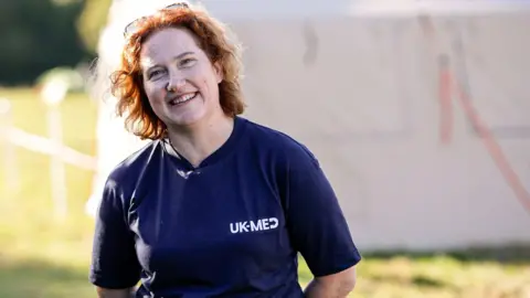 A woman in a UK-Med navy t-shirt stood outside, in front of a marquee 