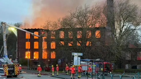 Carl Haslam/GMFRS Fire crews tackle a major fire inside the three-storey brick mill, flanked by a tower on the right. 