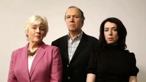 Picture shows actors from The Archers in 2007. Charles Collingwood is in the centre of the picture, flanked by his radio wife Jennifer, played by Angela Piper, on the left of the picture. Siobhan, played by Caroline Lennon, is on the right of the picture. They are all looking at the camera 