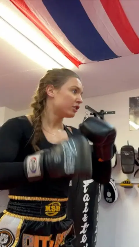 Young woman with platted hair wearing boxing gloves and boxing kit in a gym