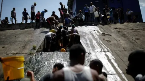 Reuters People collect water released through a sewage drain that feeds into the Guaire River, which carries most of the city's wastewater, in Caracas, Venezuela March 11, 2019.