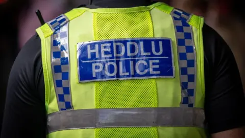 Getty Images A police officer wearing a black t-short, with their back to the camera. Their yellow vest reads 'Heddlu, Police' in a blue panel. 