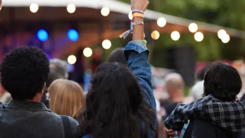 Two women are standing in front of a lit-up stage surrounded by a crowd of people.