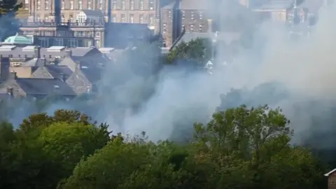 A view of smoke from behind trees in front of the backdrop of Matlock