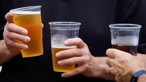 A group of hands holding plastic cups of beer. 