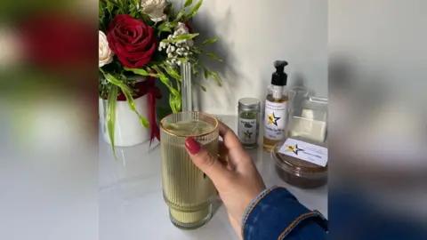 Asmaa Tayeh/Instagram A picture taken from Instagram showing a colourfully-manicured hand holding an iced coffee in front of a bouquet of roses. Plastic pots containing coffee flavourings which all have a star logo are also in the background.