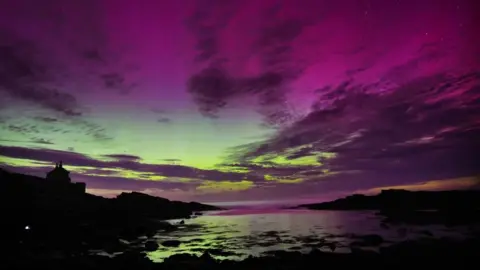 PA Media The aurora borealis, also known as the northern lights, fill the sky over The Bathing House in Howick, Northumberland in August