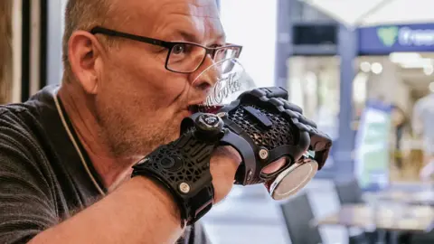 Michael Altheim pictured using the Hero Gauntlet to drink a large glass of Coca-Cola. 