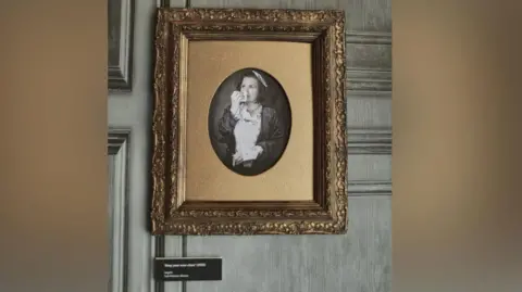 Supplied A black-and-white portrait shows a woman with short hair in a Victorian-style dress holding a handkerchief to her nose as she looks to the side. 