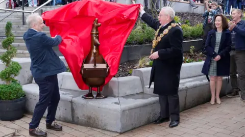 PA Media Wallace and Gromit creator Nick Park (left) and the Mayor of Preston, Councillor Phil Crowe, unveil a brown statue of the animated character Feathers McGraw at the opening of Animate in Preston.