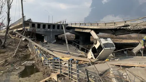 Kathy Long/BBC An overturned van on the destroyed bridge in Irpin