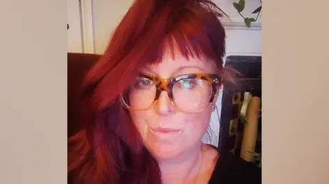 Supplied A selfie style image of a woman with long red hair and glasses. She is slightly pouting while looking directly into the camera.
