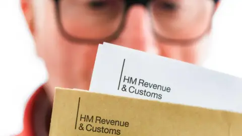 Getty Images Man in glasses in the background looking at government tax letters in the foreground