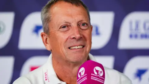 Mike Egerton/PA Wire. A man speaking into a pink microphone during a press conference, with championship branding displayed on a backdrop behind him.