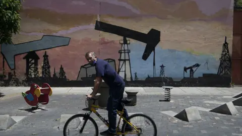 Bloomberg via Getty Images A person on a bike rides past graffiti depicting an oil drilling operation in Caracas in 2020.