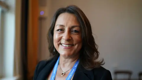 A woman is smiling in a suit. She has brown hair. 