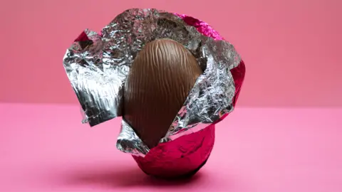 A half-uncovered chocolate egg in pink foil/
