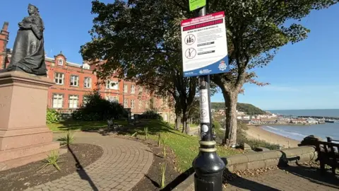 A view from a high vantage point down towards the beach and bay in Scarborough, with a sign on a pillar explaining new restrictions on street drinking in the seaside town. 