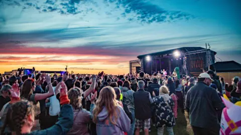 Tiree Music Festival A crowd of people looking at a stage as the sun sets in the background