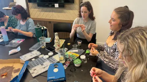 young women around a table making friendship bracelets out of beads