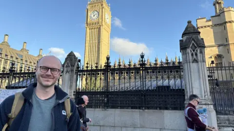 A man stands in front of Parliament with the Elizabeth Tower in the background 