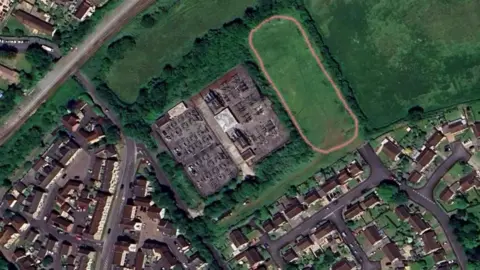 Google An aerial view showing where the proposed facility would have been built. There is a faint red line outlining a rectangular section of a field, and next to it is the existing electricity substation. There are lots of streets of residential housing nearby.