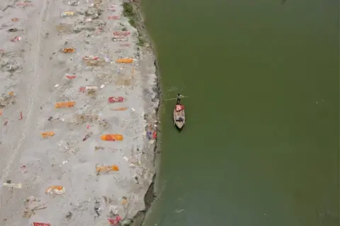 Reuters A man rows his boat past shallow sand graves of people, some of which are suspected to have died from the coronavirus disease (COVID-19), on the banks of the river Ganges in Phaphamau on the outskirts of Prayagraj, India, May 21, 2021