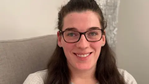 George King/BBC A head and shoulders image of Hannah Dickerson. She is wearing glasses and looking directly into the camera while smiling.