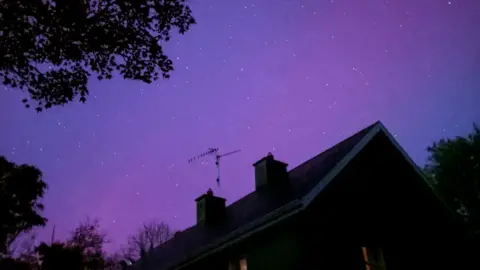 A purple sky from the Northern Lights, with the roof of a house in the bottom half of the image