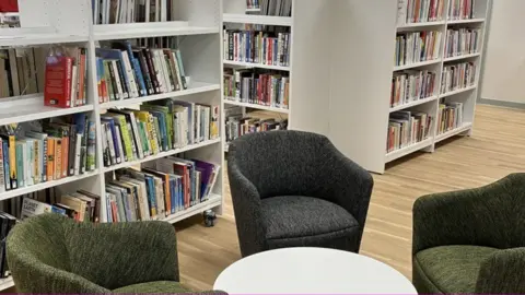 Biggleswade Library Chairs placed around a small white round table in a library. There are shelves of books in the background.