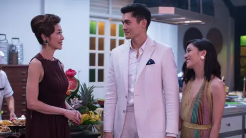 Warner Brothers Movie still from Crazy Rich Asians showing Michelle Yeoh, Henry Golding and Constance Wu smiling at one another