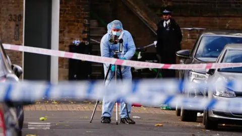 A police forensic officer behind a cordon on Southern Grove in Ladbroke Grove