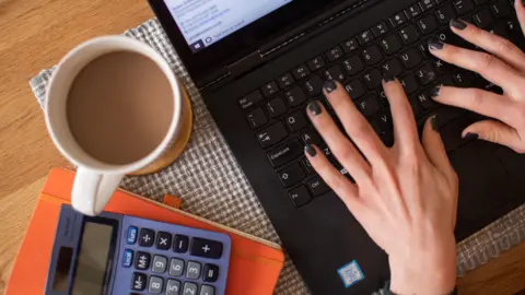 Generic of person typing on laptop with calculator and cup of tea